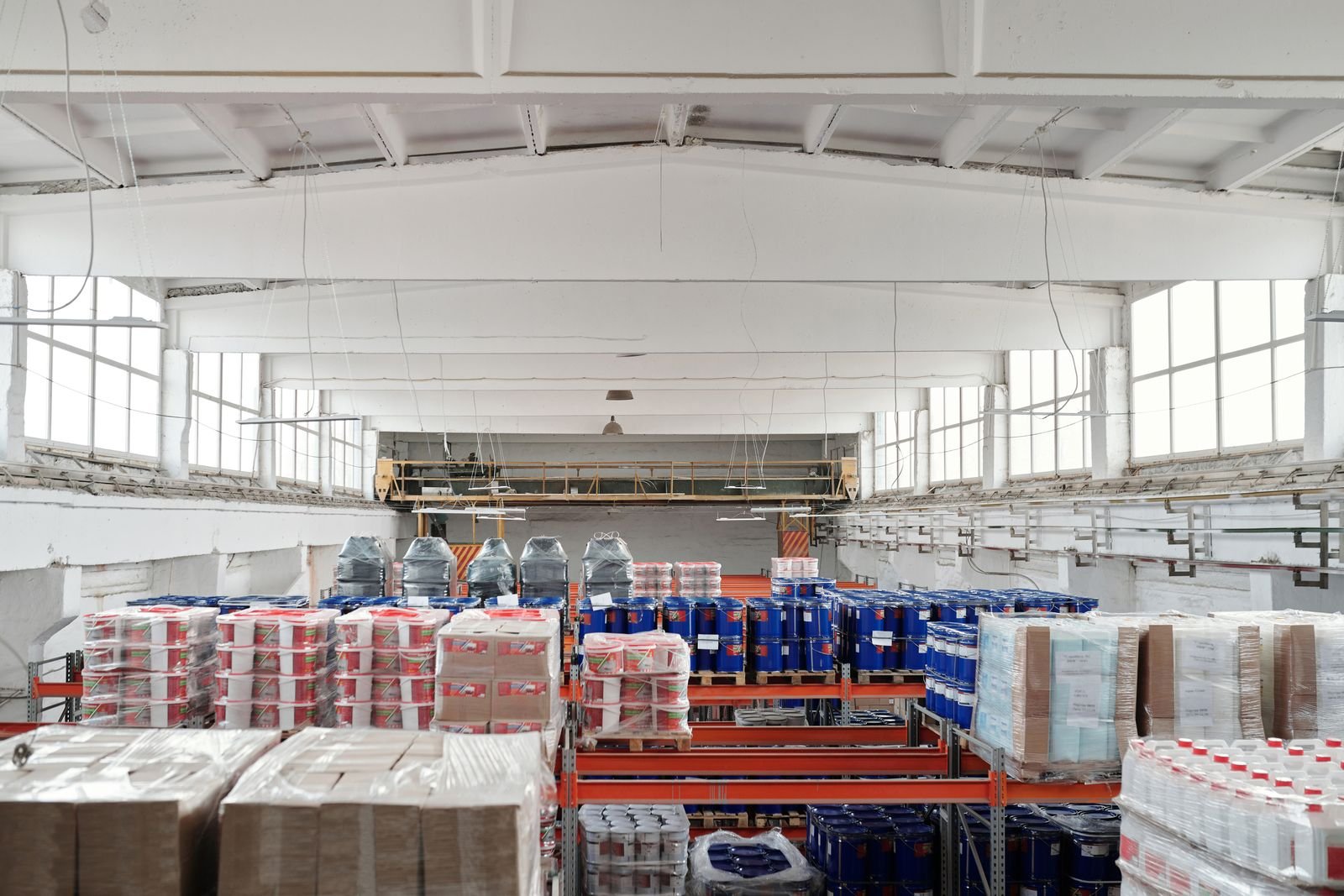 A wide, bright storage hall with stacked goods and workers moving them