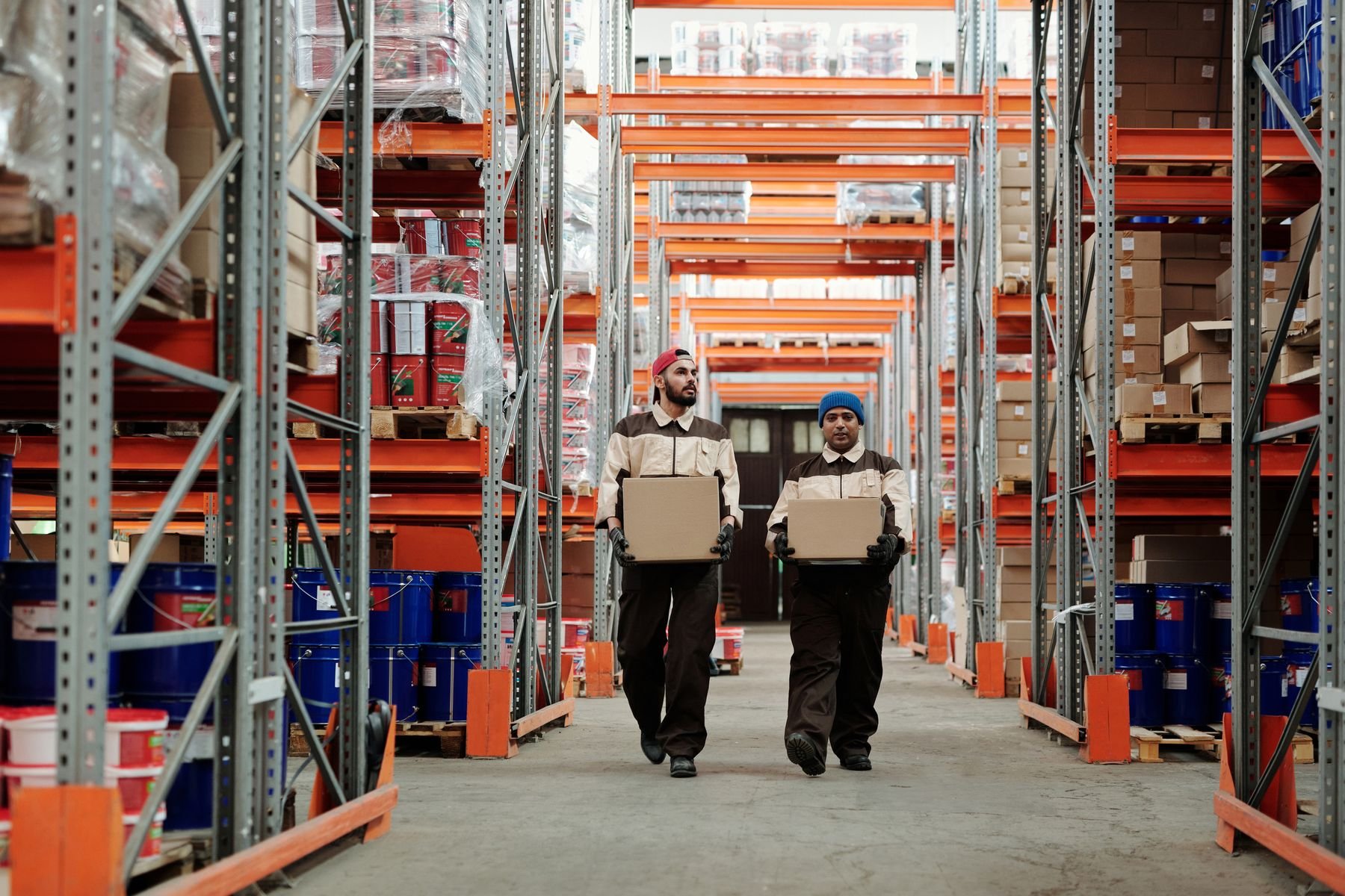 Two warehouse workers carrying boxes along a racked aisle